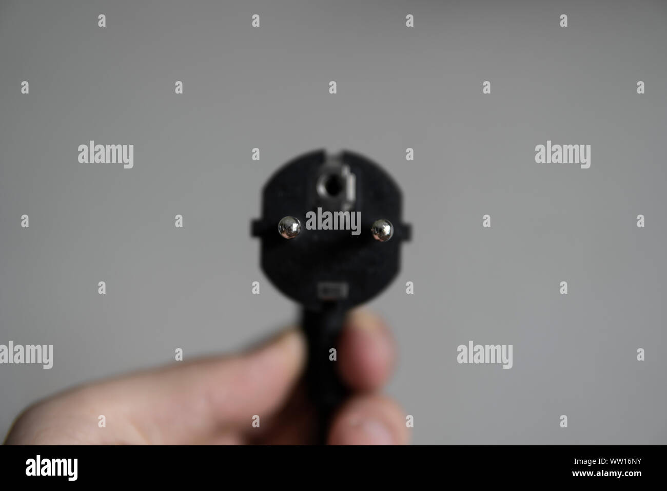 Hand holding black electric plug on a grey background. Stock Photo