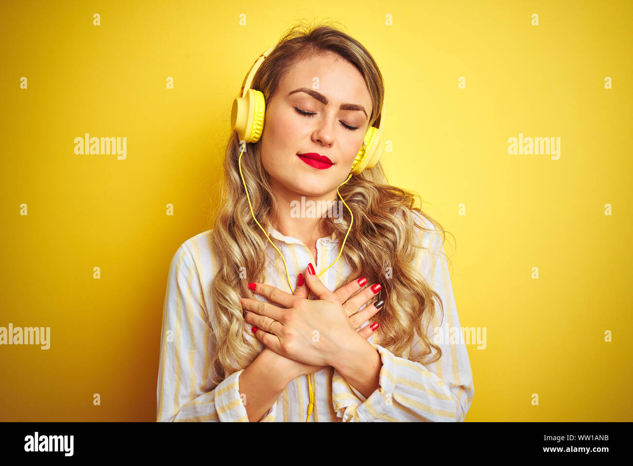 Young beautiful woman listening to music using headphones over yellow ...