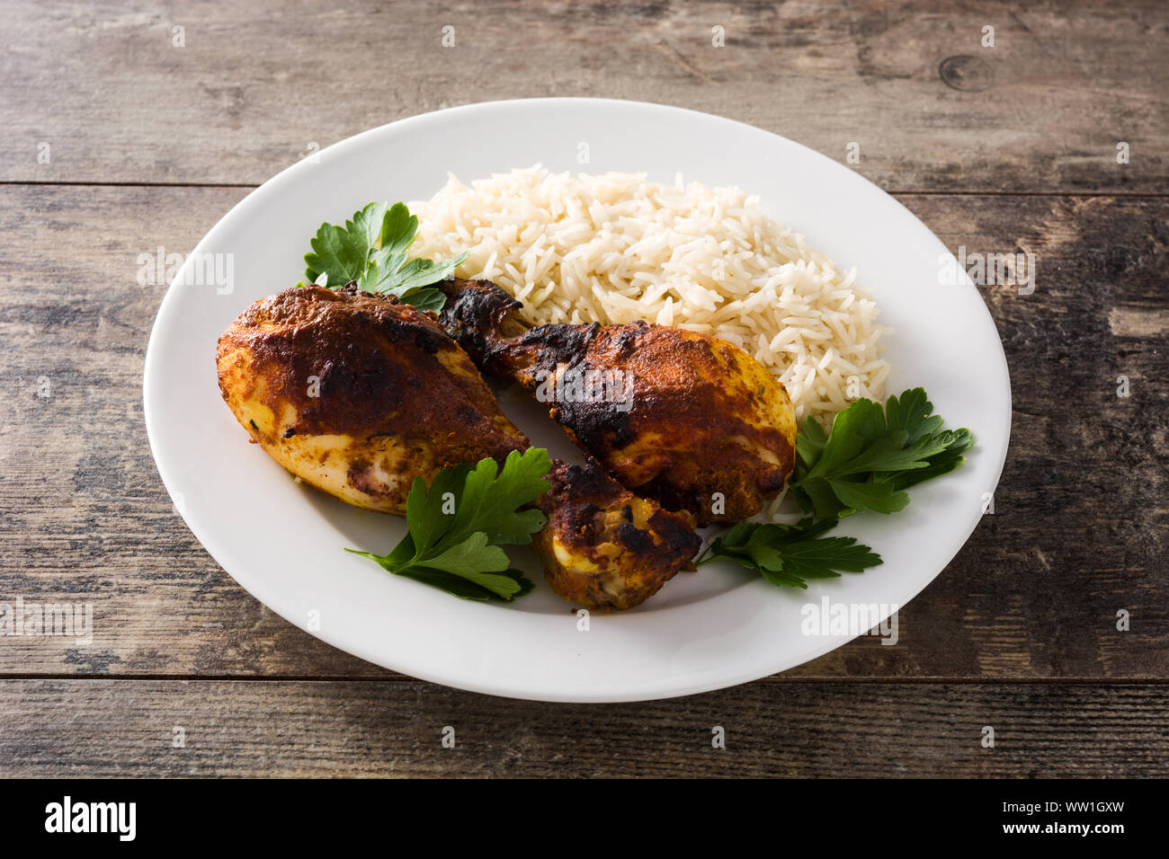 Roasted tandoori chicken with basmati rice in plate on wooden table ...