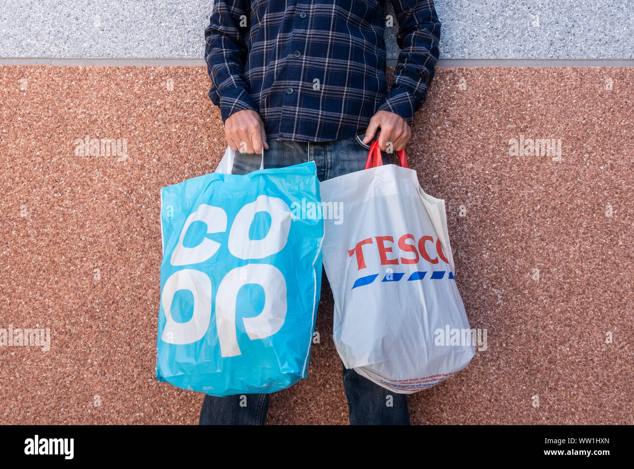 Man holding Coop and Tesco supermarket plastic shopping bags. UK Stock Photo