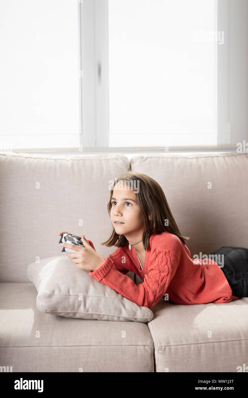 Niña jugando en casa con la videoconsola tumbada en el sofá Stock Photo