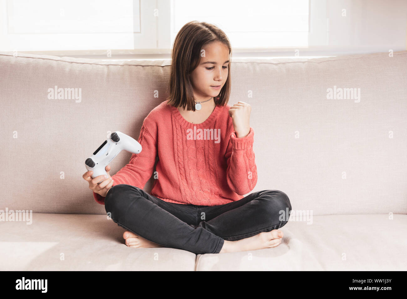 Niña jugando en casa con la videoconsola sentada en el sofá Stock Photo