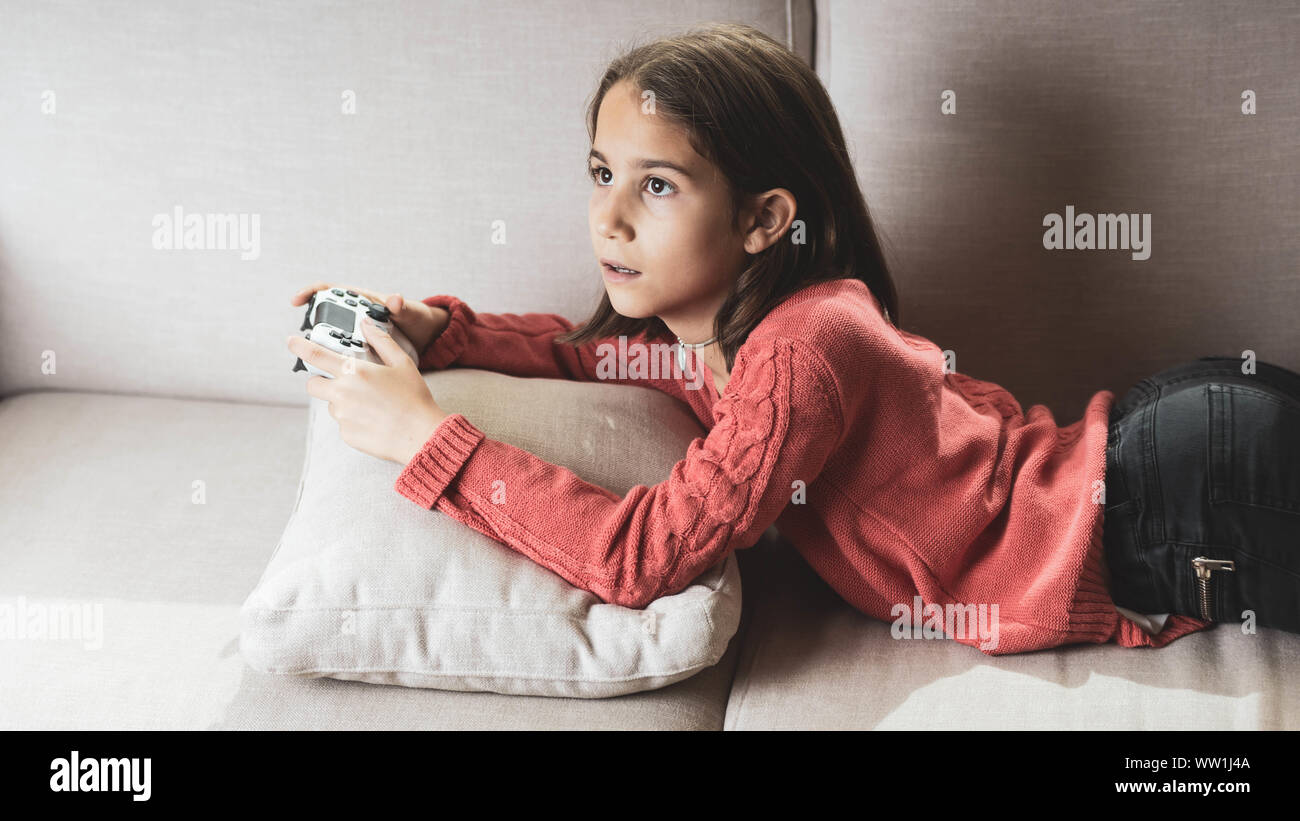 Niña jugando en casa con la videoconsola tumbada en el sofá Stock Photo