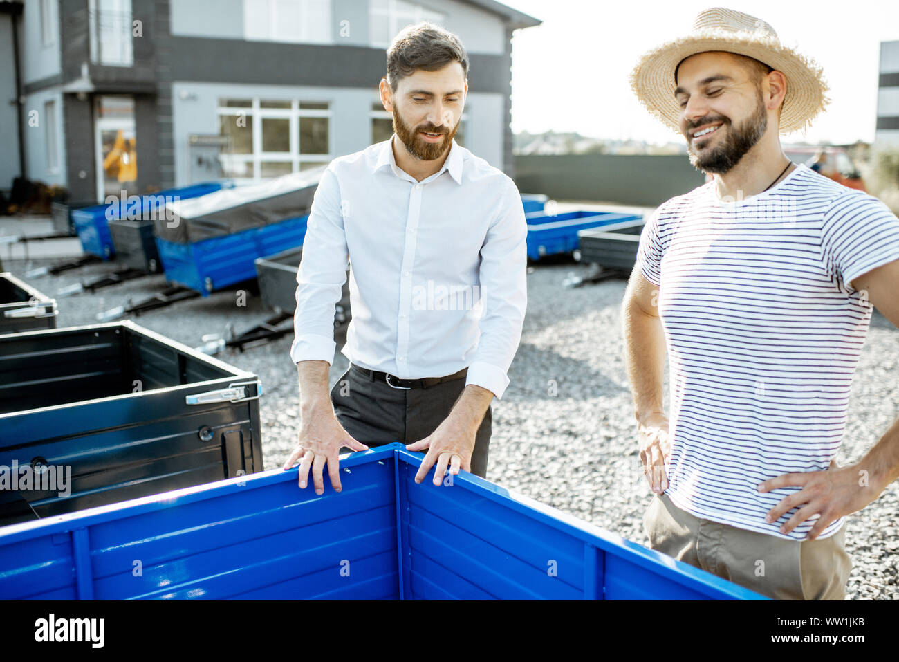 Agronomist with salesman choosing a new farm truck trailer, standing on