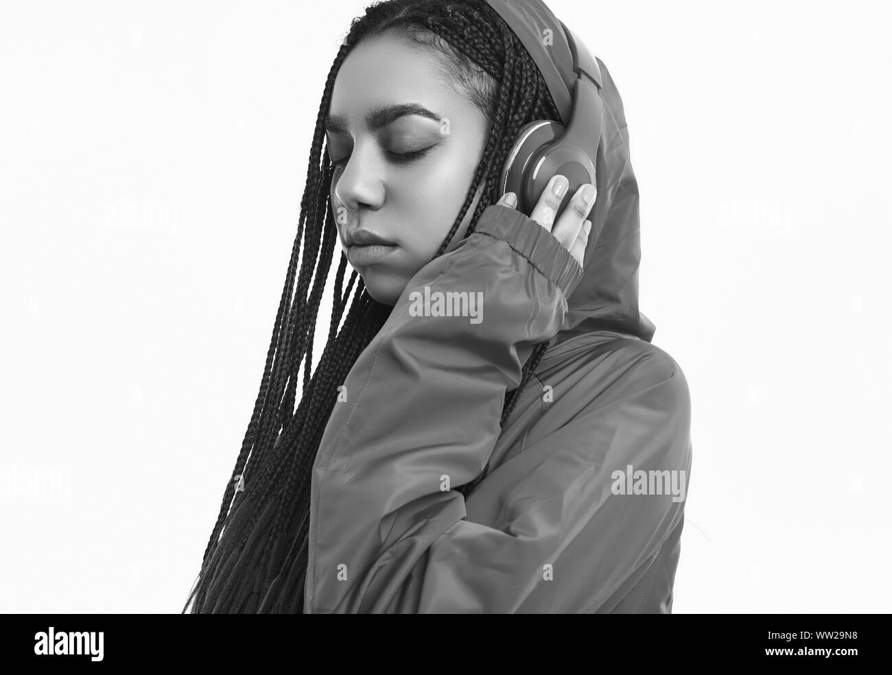 Portrait of beautiful african brunette teenage girl with dreadlocks wearing a red windbreaker listening music via wireless headphones isolated on stud Stock Photo