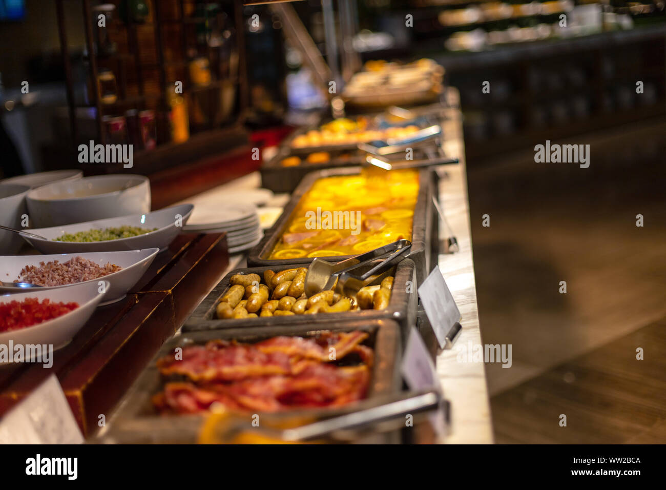 Buffet breakfast at a Chinese hotel. Focus on sausages on blurry background of food trays. Breakfast is included in the hotel. Stock Photo
