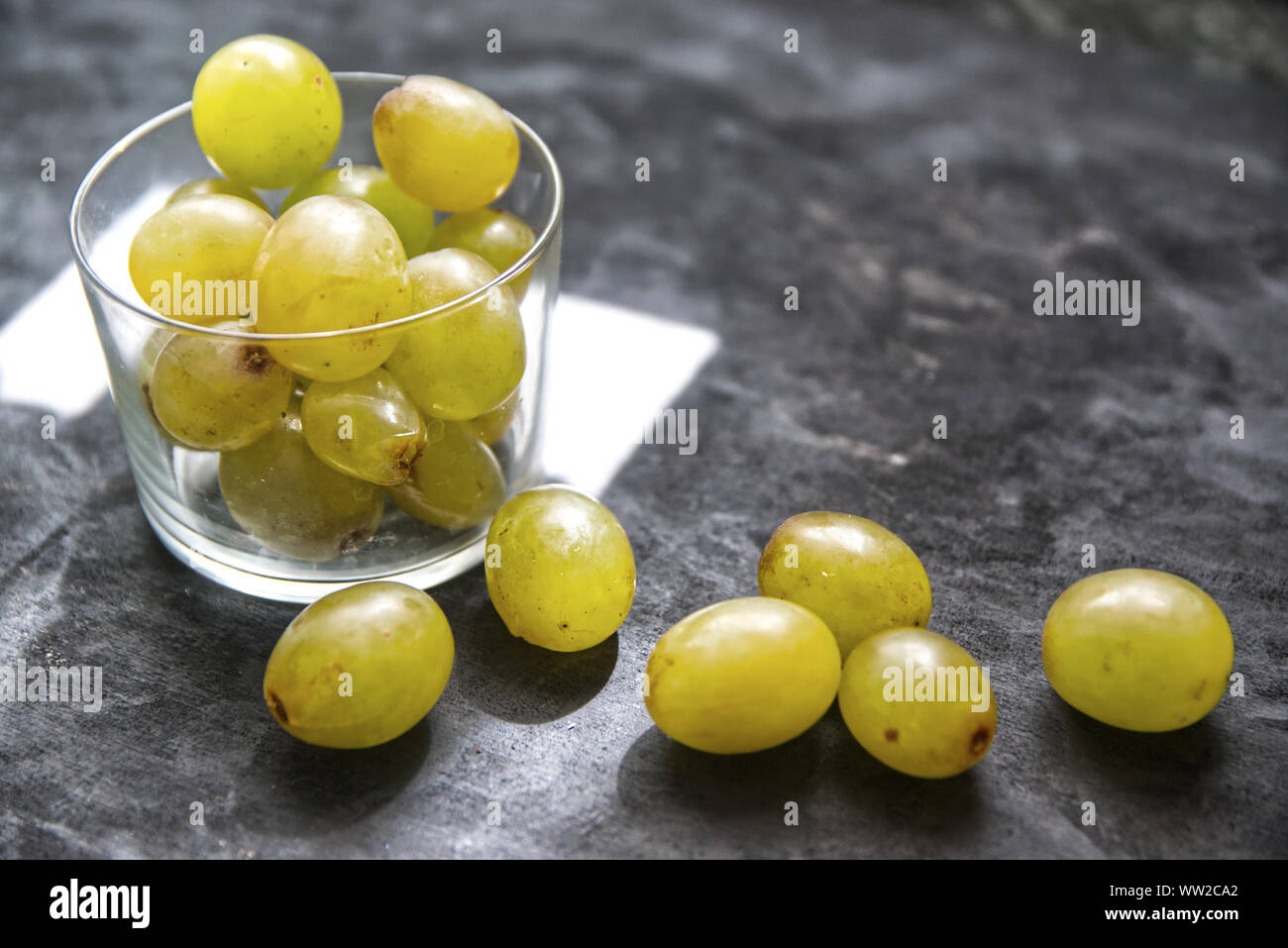 Some white grapes ready for winery in a glass on a black wooden table of a rustic kitchen. Empty copy space for Editor's text. Stock Photo