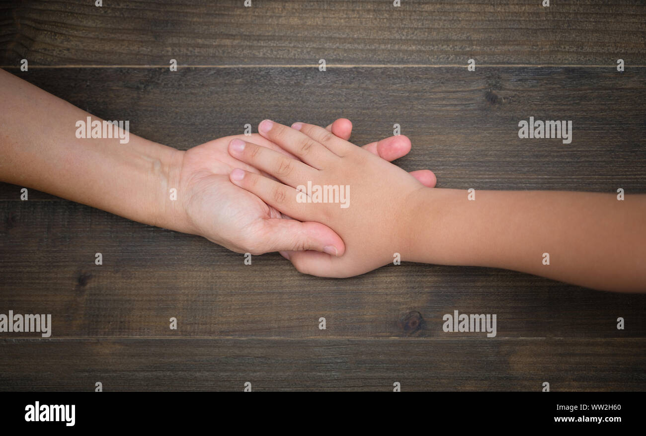 Hands of mother and child on dark brown wooden table background, Flat lay style with copy space to write, lowkey or dark light. Stock Photo