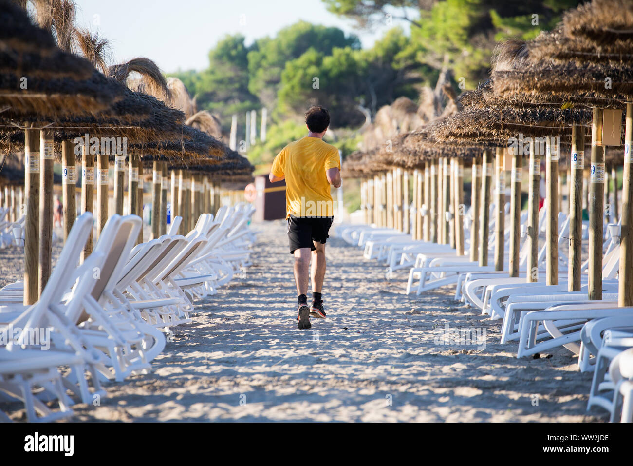 Unrecognizable runner between sunbeds and umbrellas on beach near Alcúdia, Mallorca Stock Photo