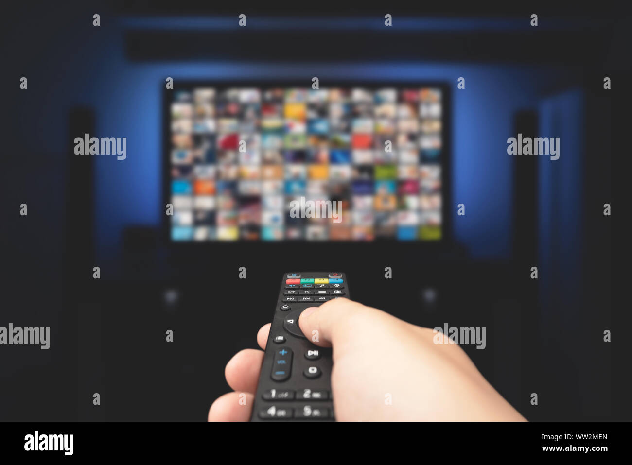 Multimedia video concept on TV set in dark room. Man watching TV with remote control in hand. Stock Photo