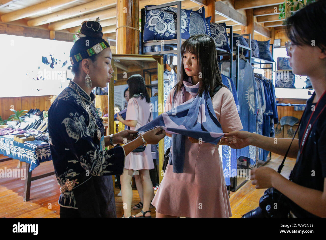 (190912) -- BEIJING, Sept. 12, 2019 (Xinhua) -- Zhang Yiping (1st L) from "Mom Handworks Cooperative" introduces a batik scarf to a tourist at a batik craft cooperative of "Mom Handworks" in Danzhai County, southwest China's Guizhou Province, Aug. 23, 2019. "Mom Handworks" is a public welfare project initiated by China Women's Development Foundation (CWDF) in September 2016. About 46 "Mom Handworks Cooperatives" have been established in 13 provinces nationwide. The project helps create jobs for poverty-stricken mothers and provide them with some handcraft skills to make handicrafts with local Stock Photo
