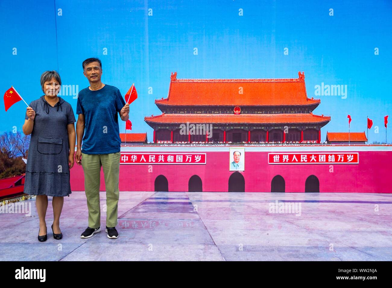 Local Chinese residents wave Chinese national flags in front of a backdrop showing the Tiananmen Rostrum during a campaign to celebrate the 70th anniv Stock Photo