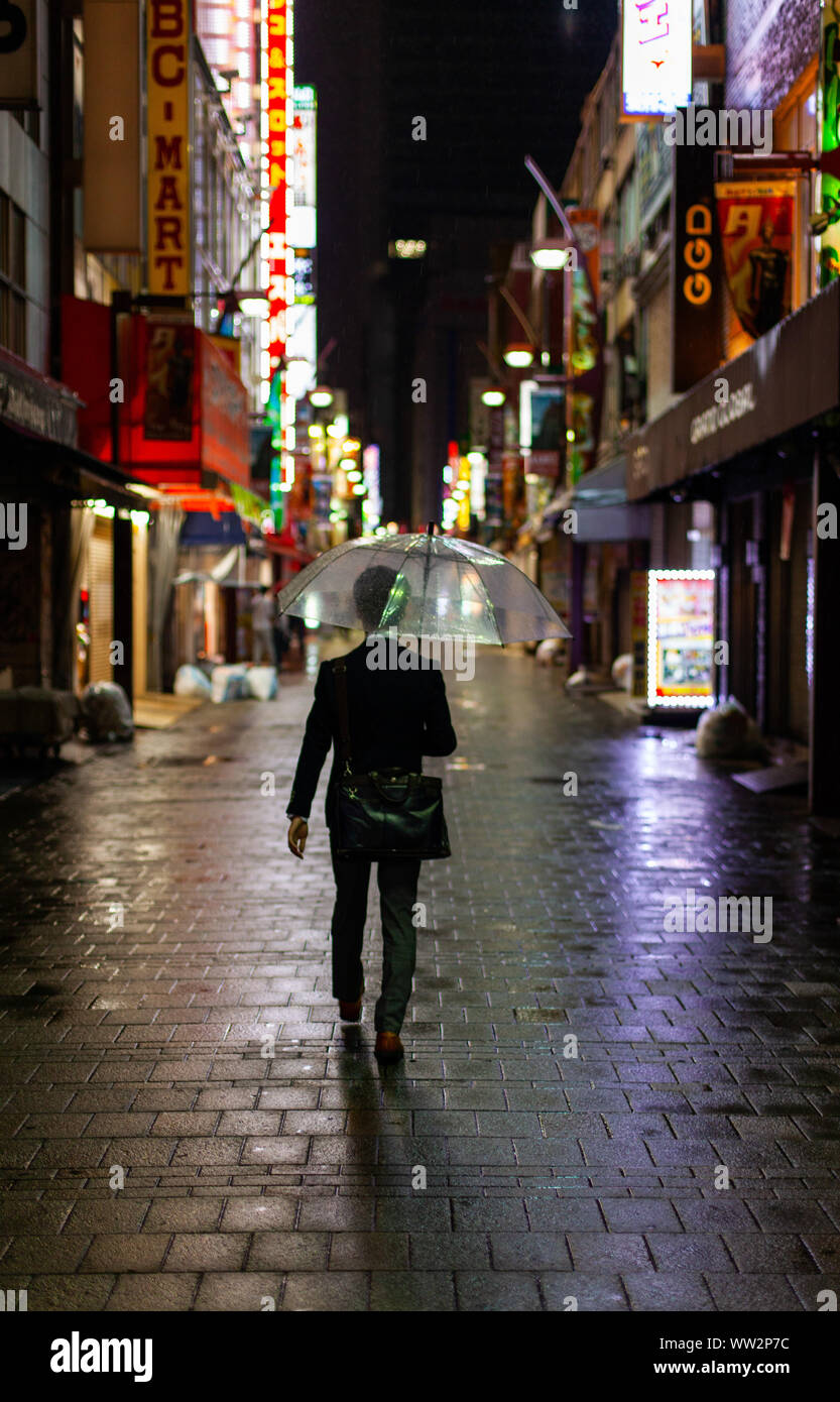 Man walking in rain with umbrella at night Stock Photo