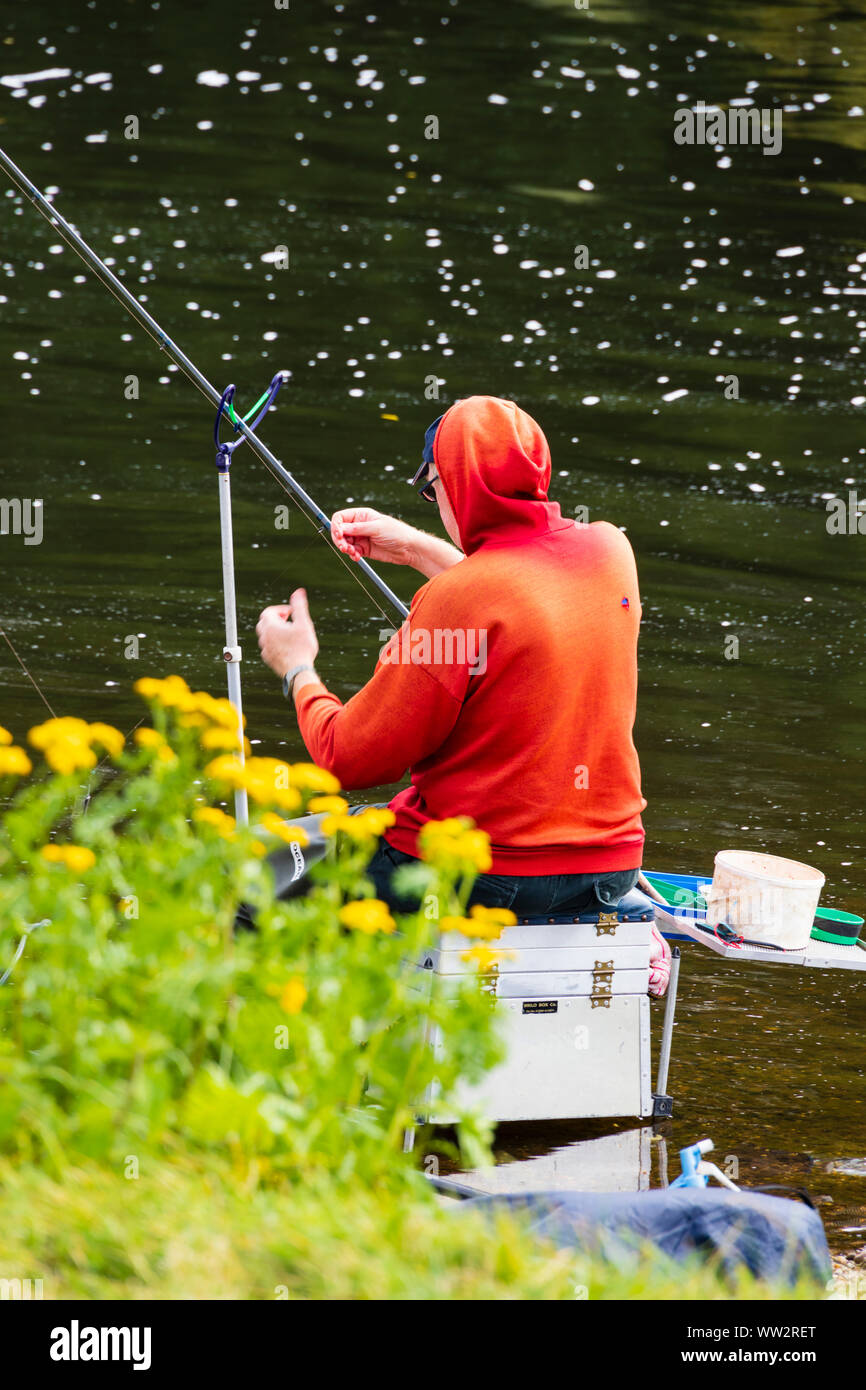 A man in a bright red jacket, fishing in the River Trent, Gunthorpe, Nottinghamshire. Stock Photo