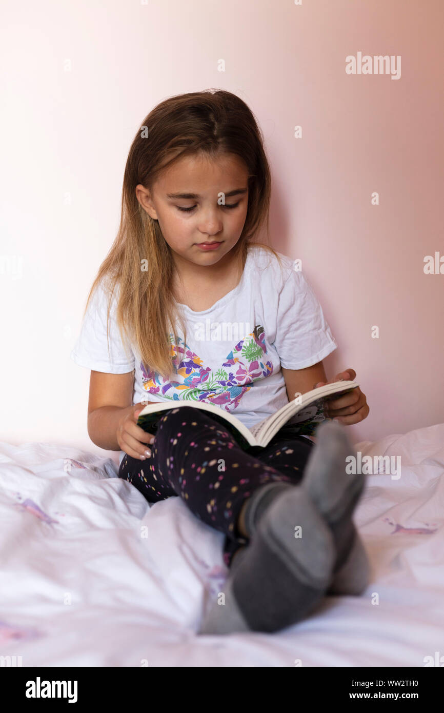 A girl aged 8 reading a book in her bedroom Stock Photo