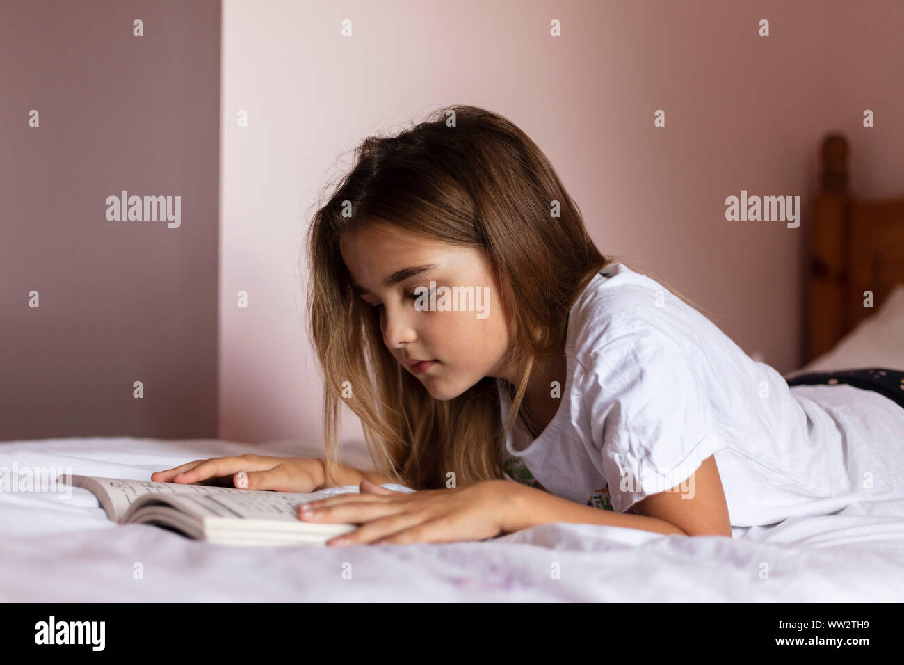 A girl aged 8 reading a book in her bedroom Stock Photo