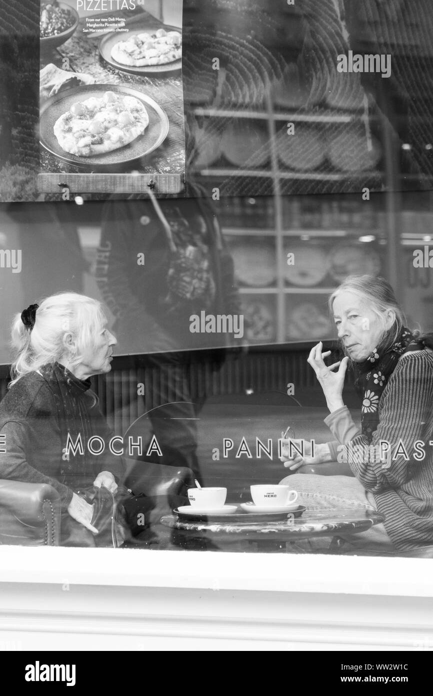 Two senior women sat by a window enjoying a cup of coffee in a cafe, York, North Yorkshire, England, UK. Stock Photo