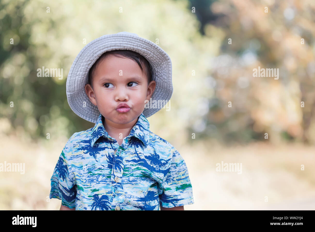 Cute young boy wearing a tropical print shirt and hat who is blowing kisses while looking away to the distance. Stock Photo