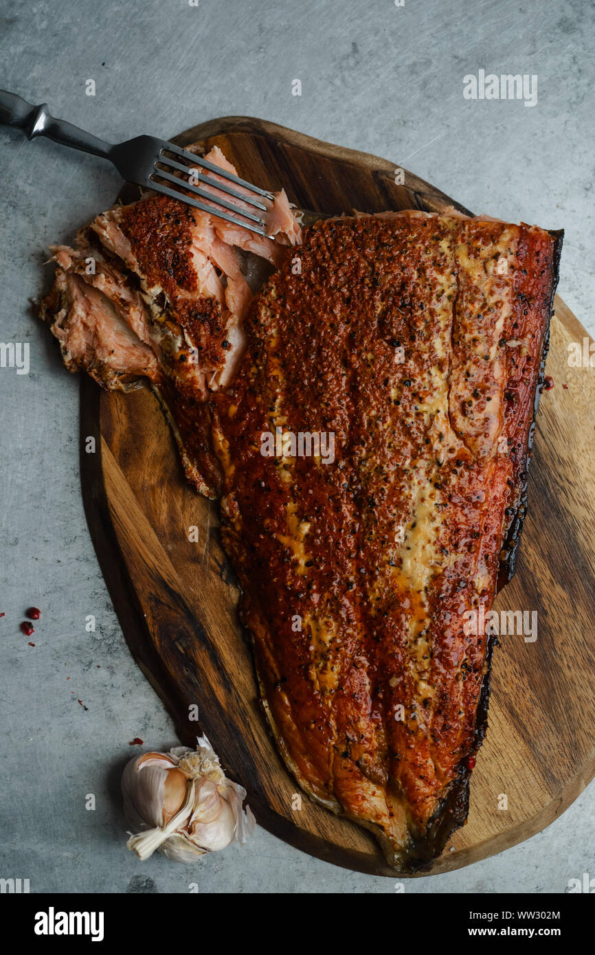 Smoked salmon with pepper on wooden cutting board on metallic surface ...