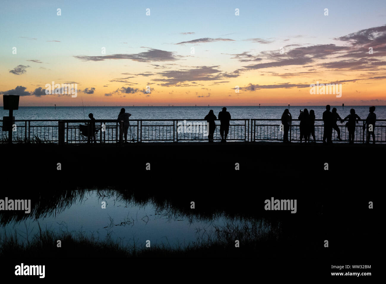 Silhouettes of people standing at the waterside watching the sunset at Hudson Beach, Florida Stock Photo