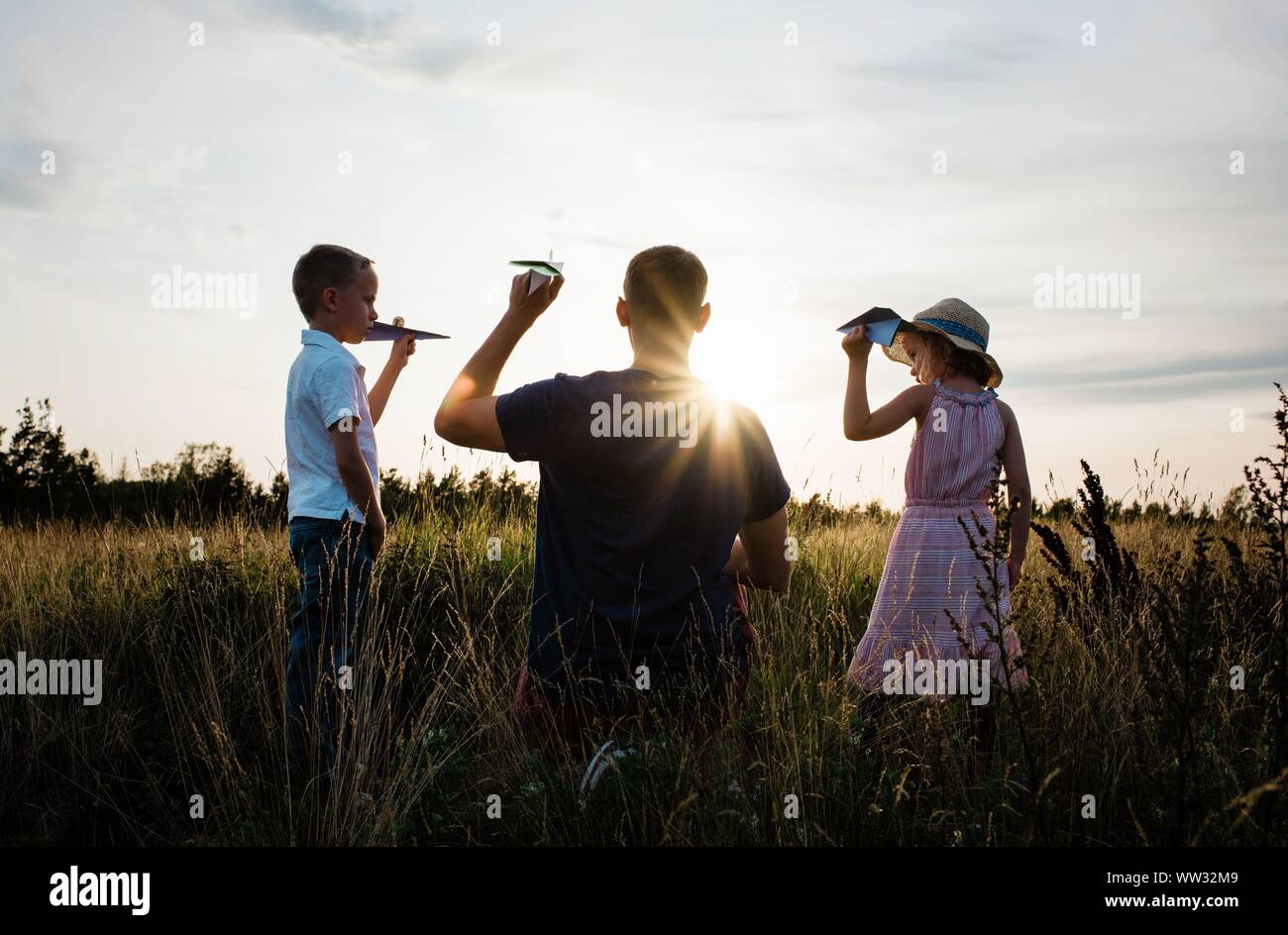 father playing with his son and daughter in a meadow at sunset Stock Photo