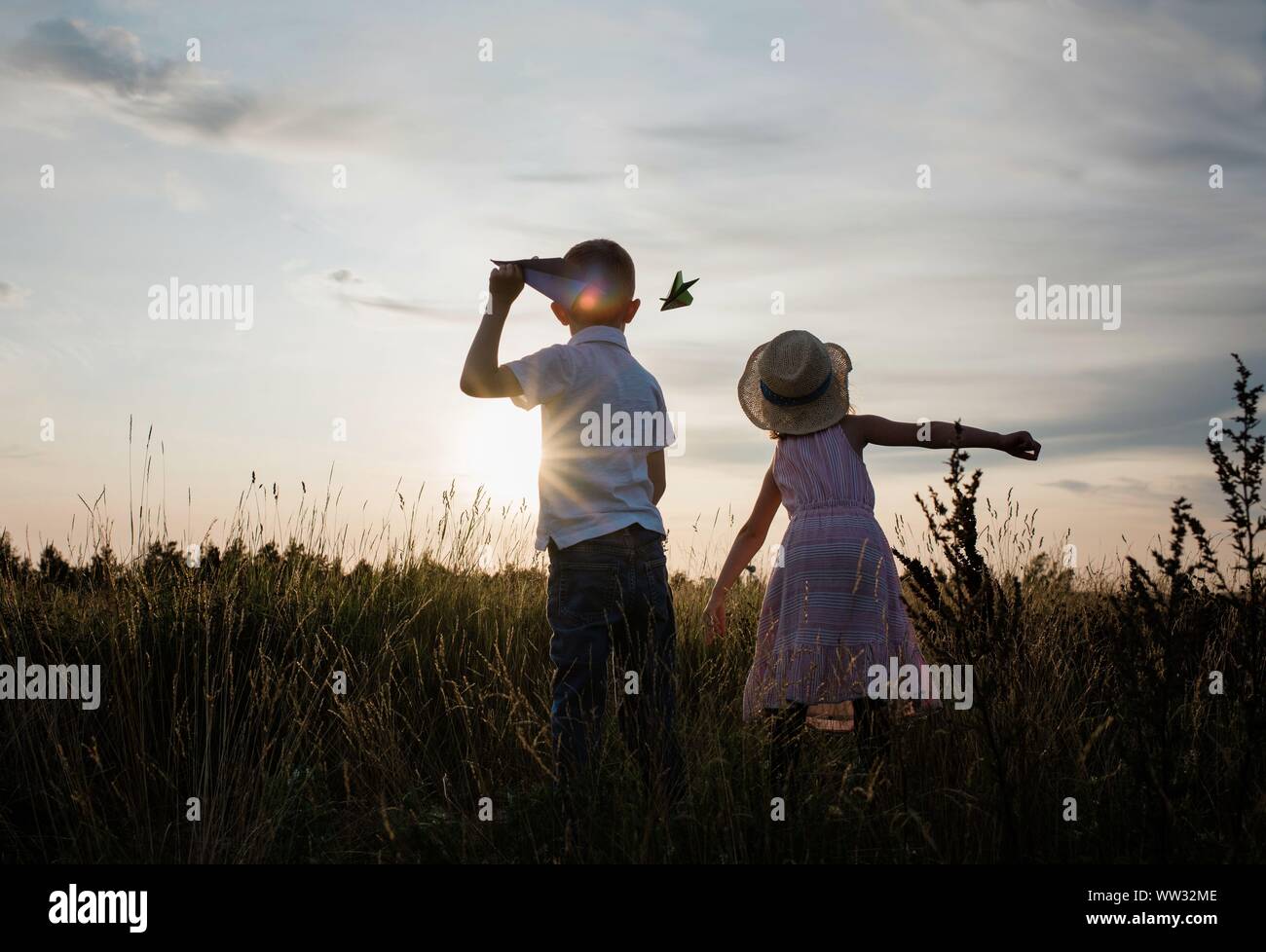 brother and sister flying planes playing in a meadow at sunset Stock Photo