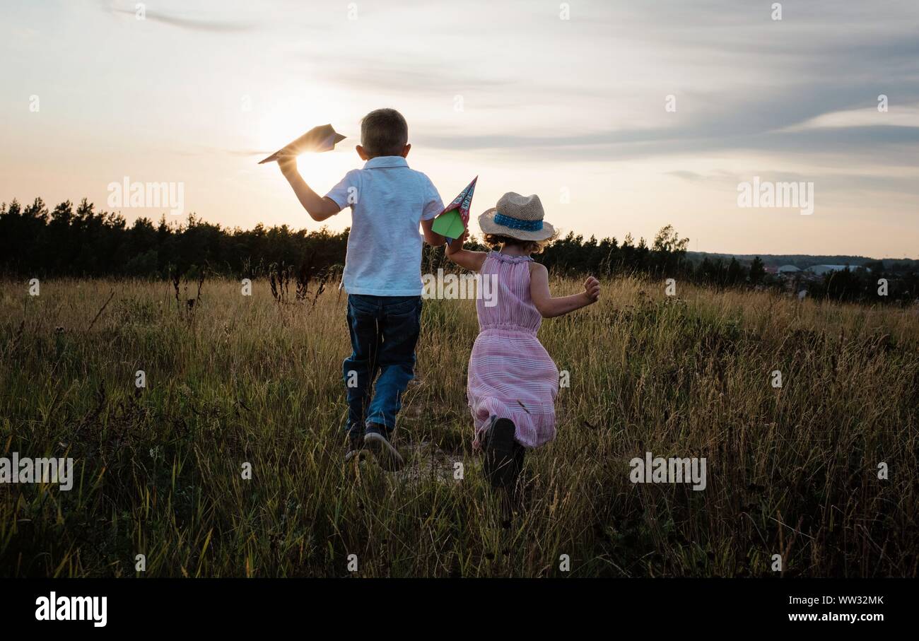 siblings running through a meadow together playing at sunset Stock Photo