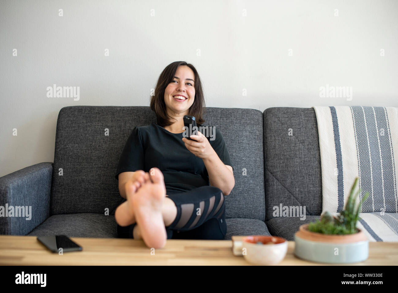 Woman Sitting On Couch With Feet Up With Remote Stock Photo Alamy