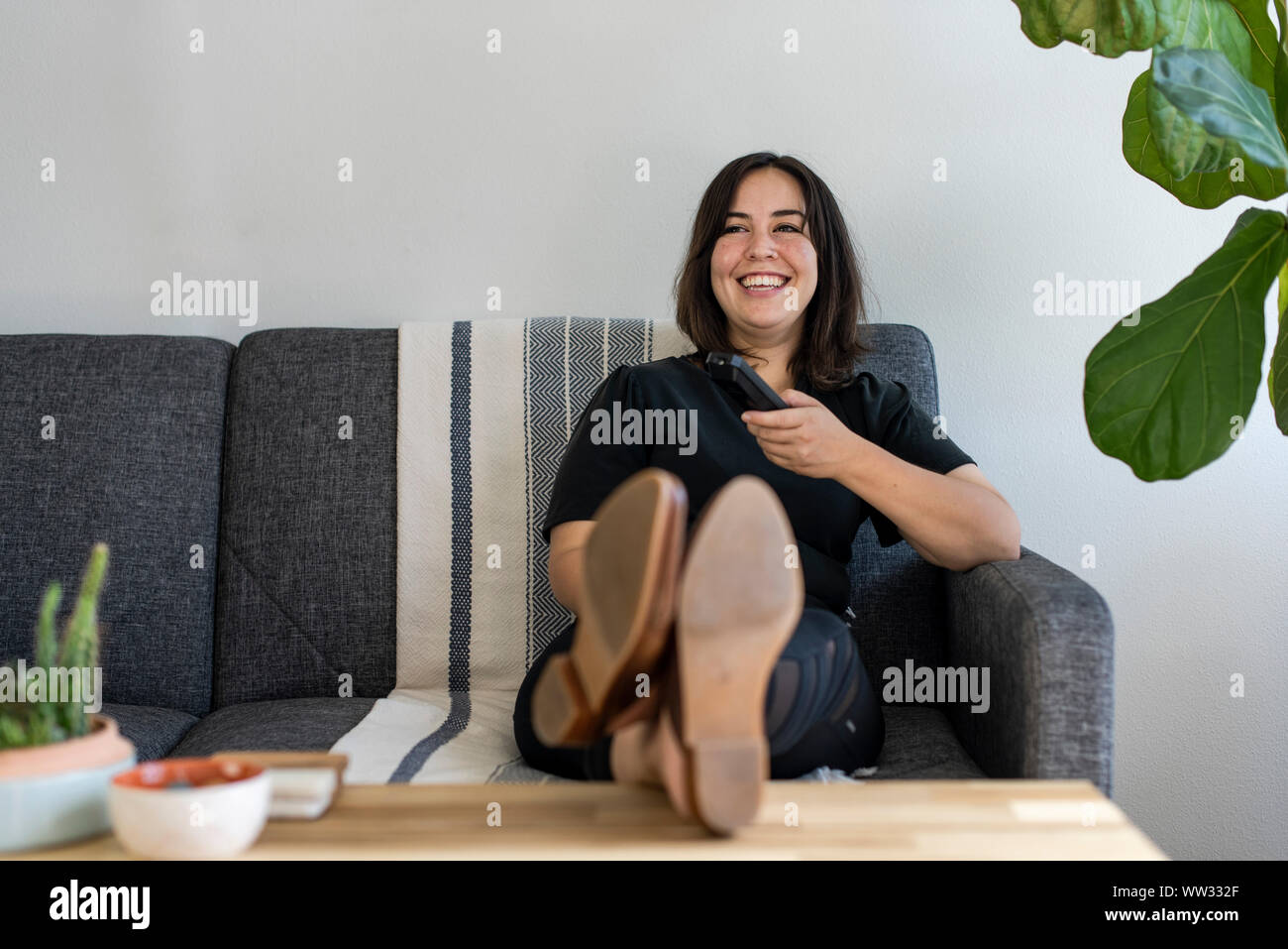 Woman sitting on couch holding remote control Stock Photo