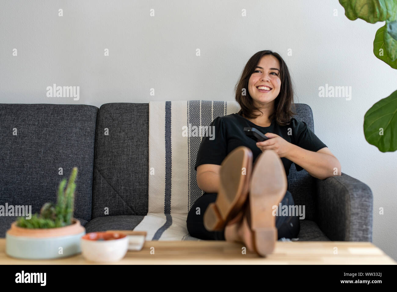 Home holding remote control sitting on couch Stock Photo