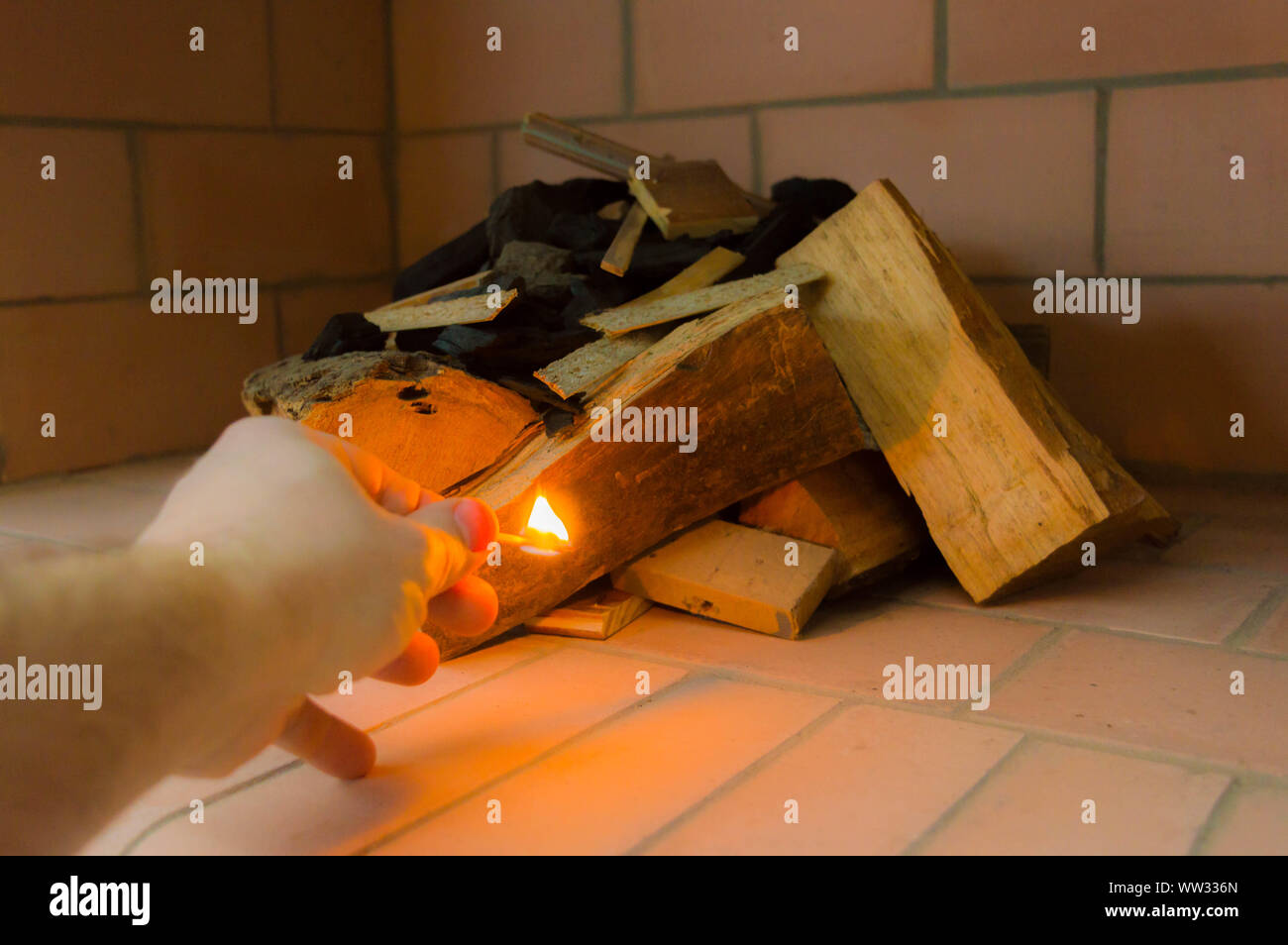 A hand with a burning match giving fire to some logs. Stock Photo