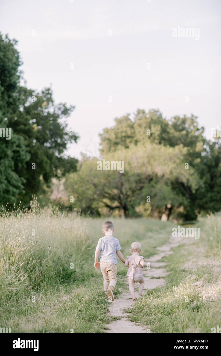 Big brother and baby sister holding hands and walking in nature Stock Photo