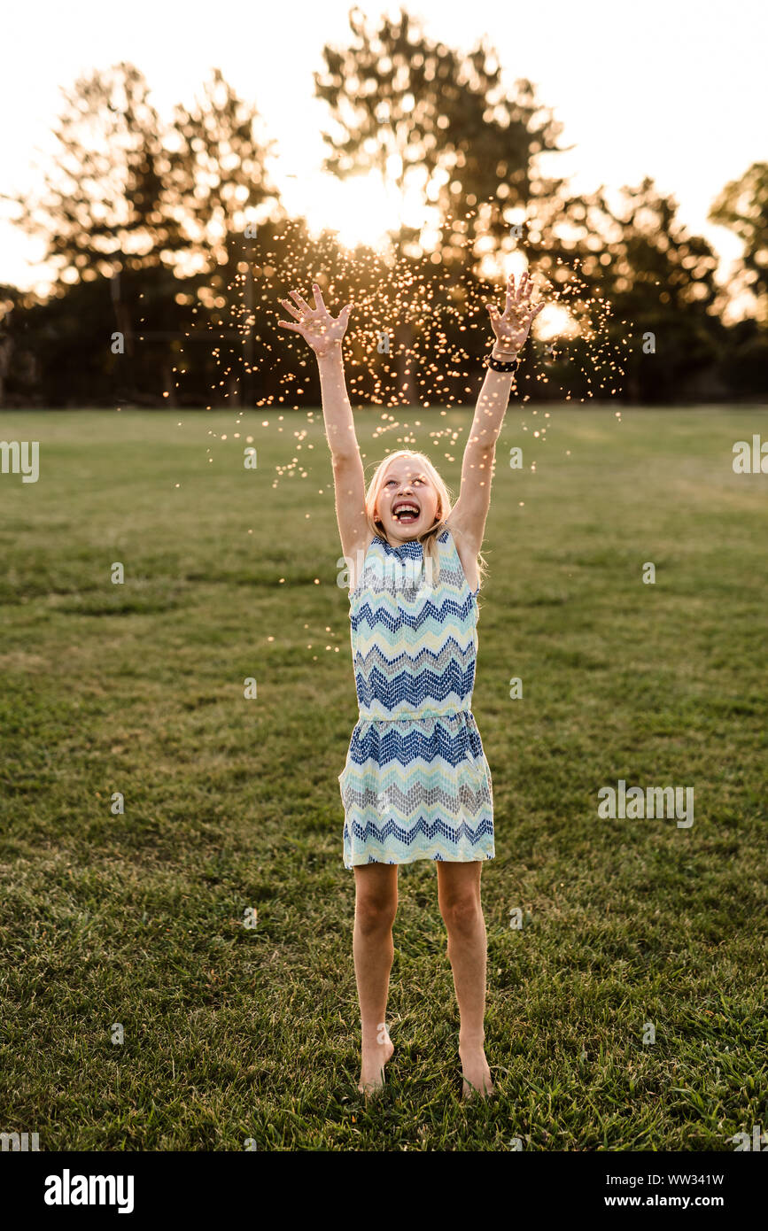 Happy tween girl throwing flowers in air at dusk Stock Photo