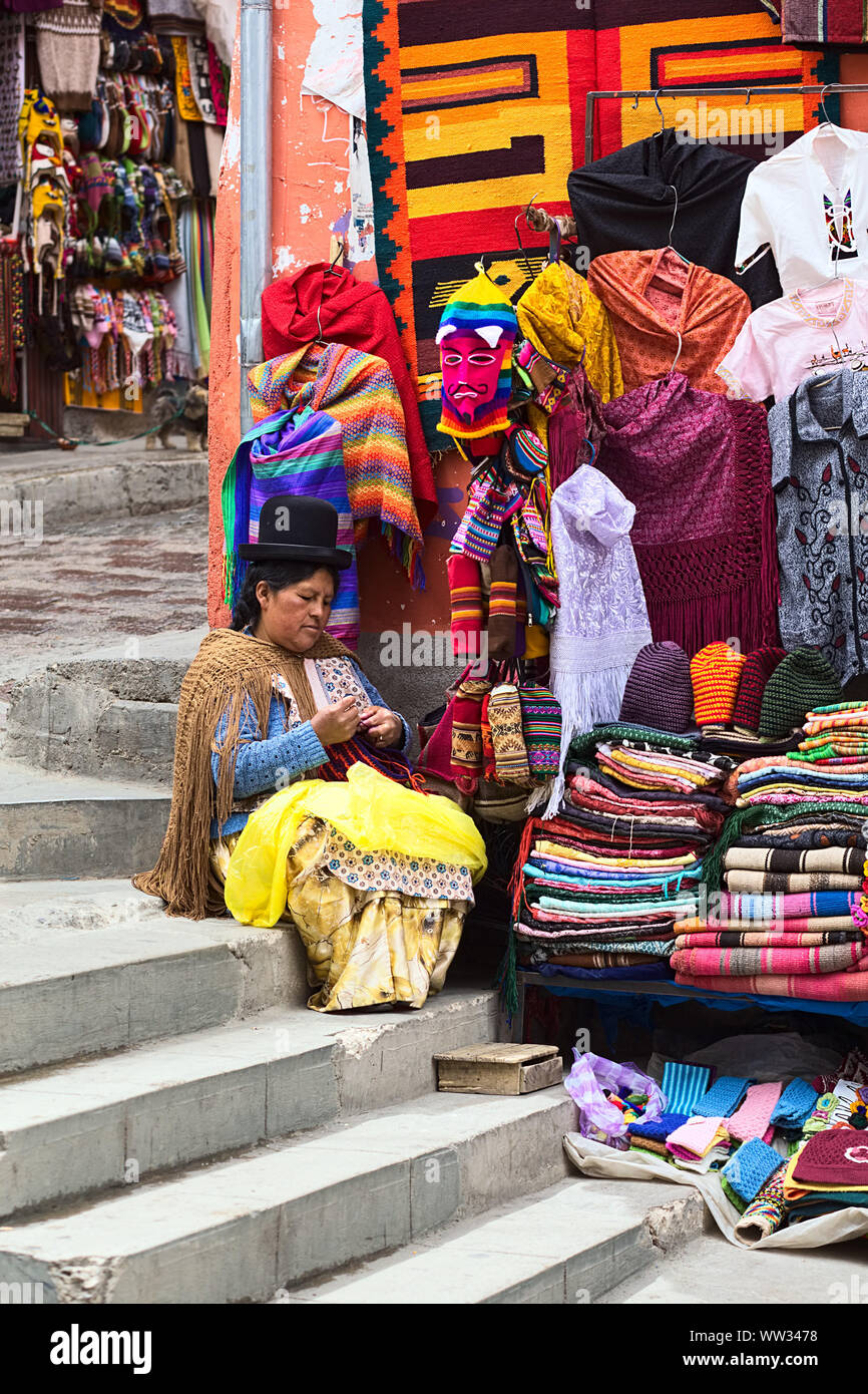 LA PAZ, BOLIVIA - NOVEMBER 10, 2014: Unidentified woman doing crochet sitting on the stairs beside her small street stand on the corner Stock Photo
