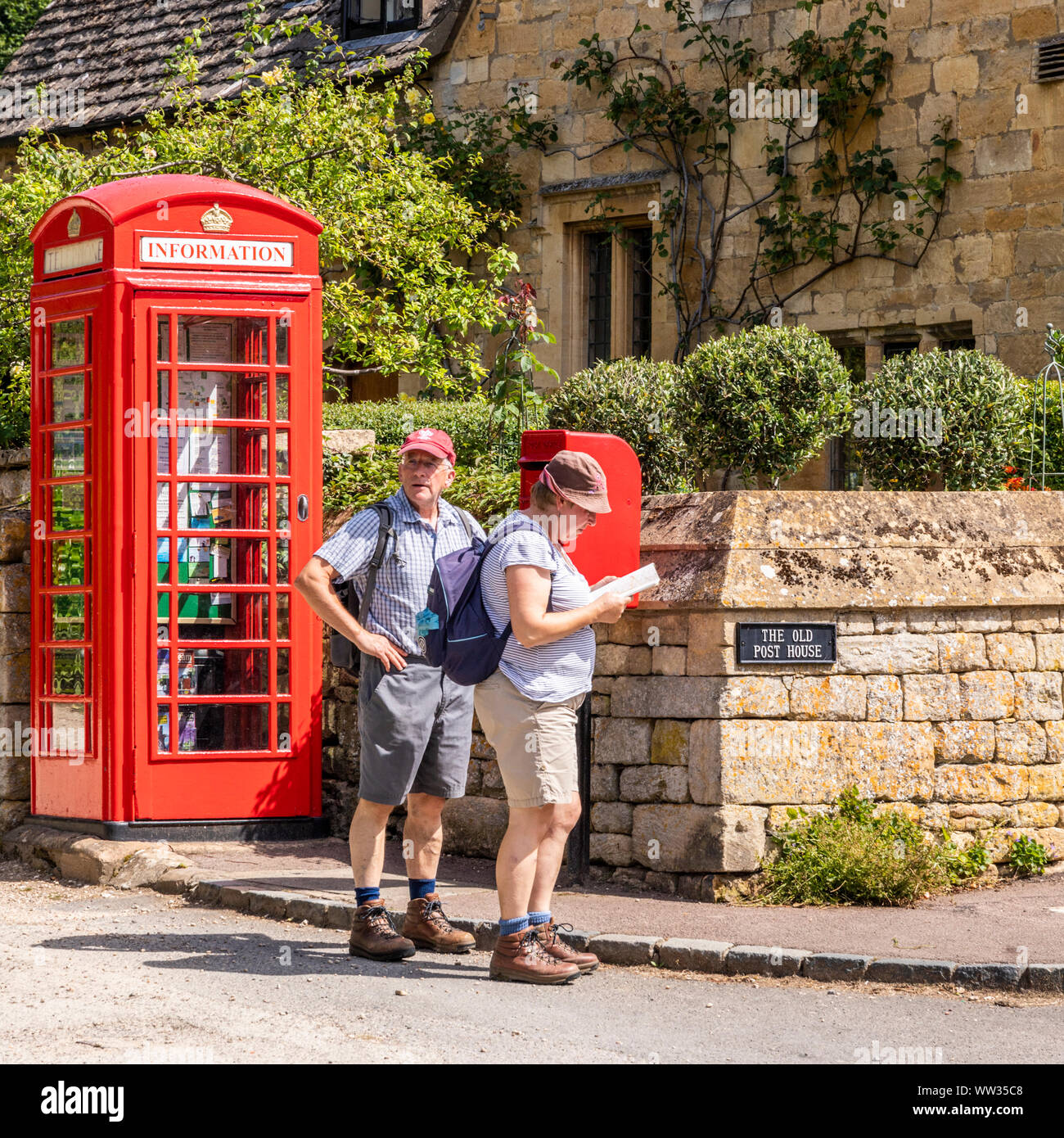 A couple of senior hikers walking the Cotswold Way stop to read the map beside the red telephone box now converted into an information point in the Co Stock Photo