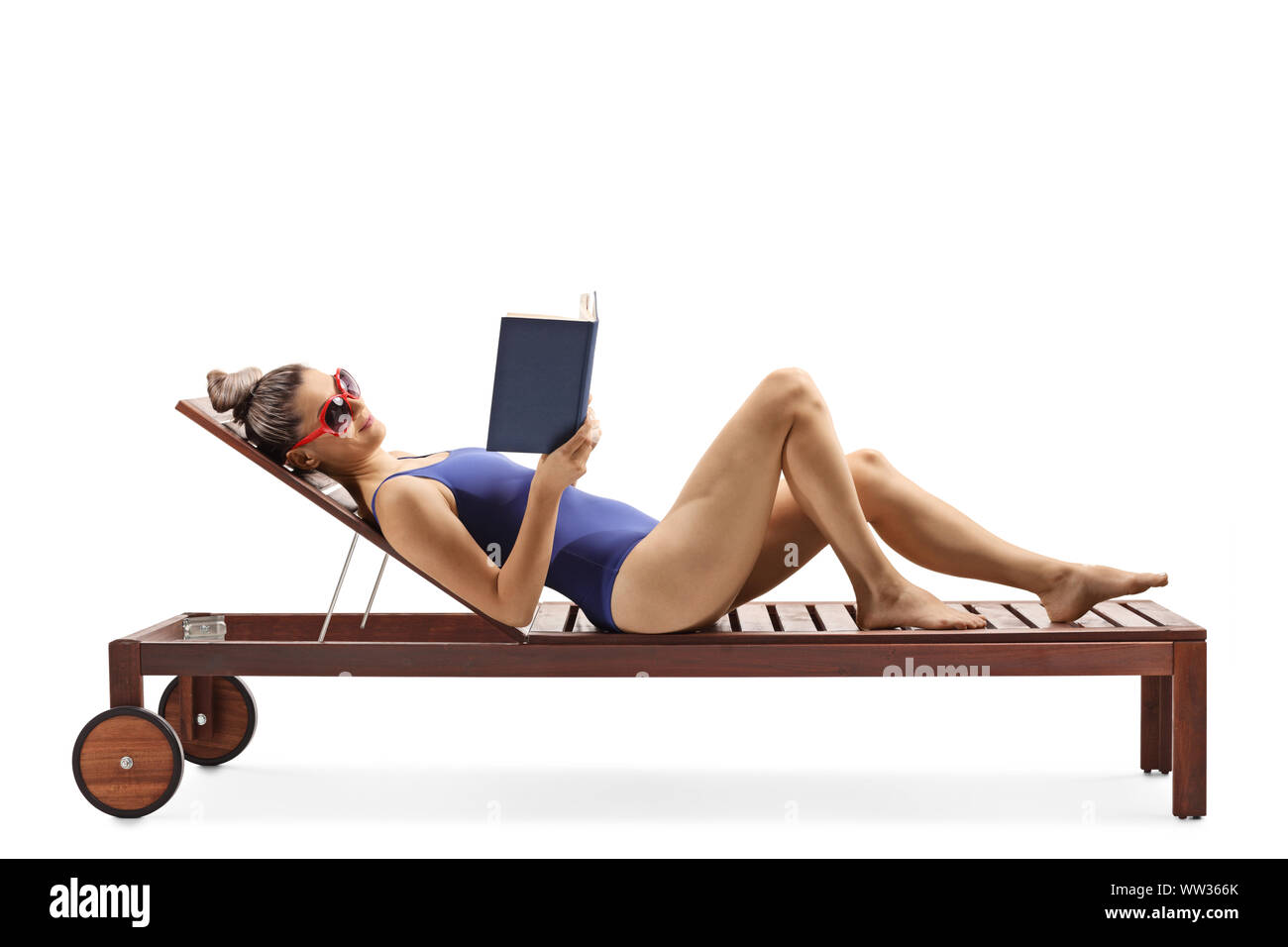 Full length profile shot of a young female in a swimsuit lying on a lounge chair and readng a book isolated on white background Stock Photo