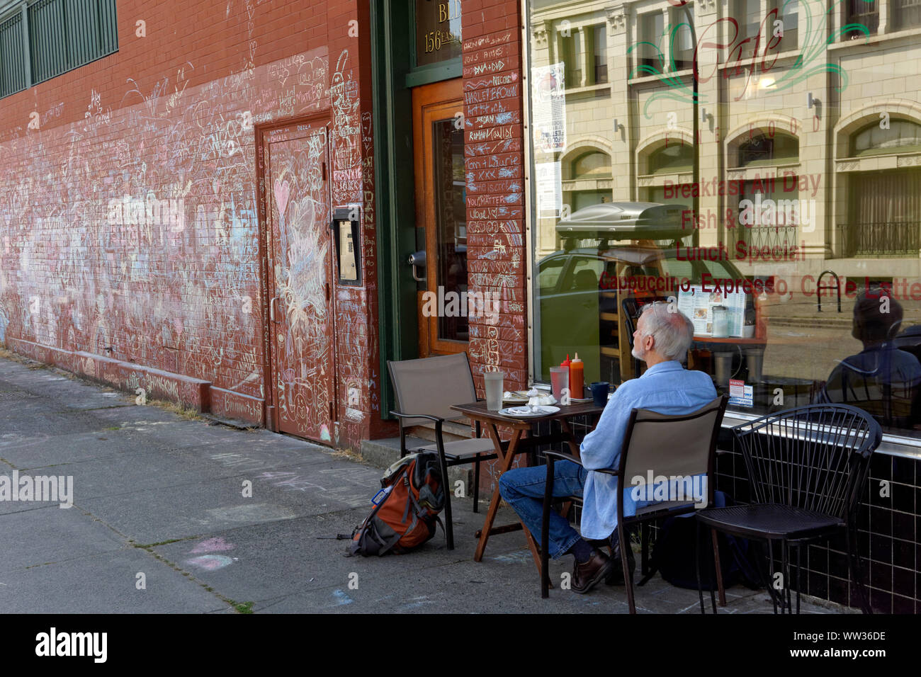 Older man sitting alone at a table outside a restaurant cafe in the Mount Pleasant district of Vancouver, BC, Canada Stock Photo