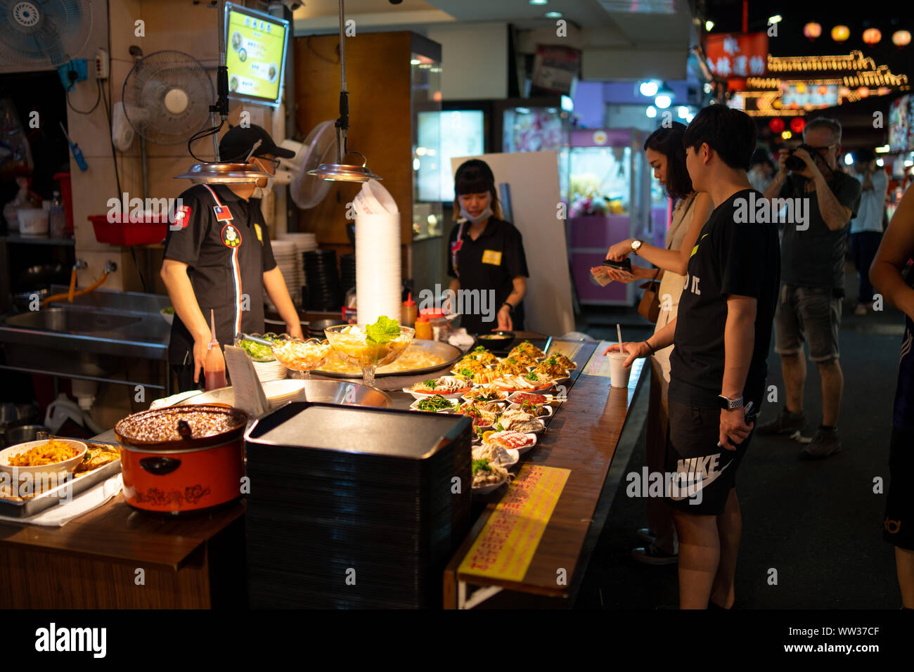 Taipei: Customers buying food of a street food vendor. Street food stall selling a variety of different dishes at sidewalk buffet at a night market Stock Photo