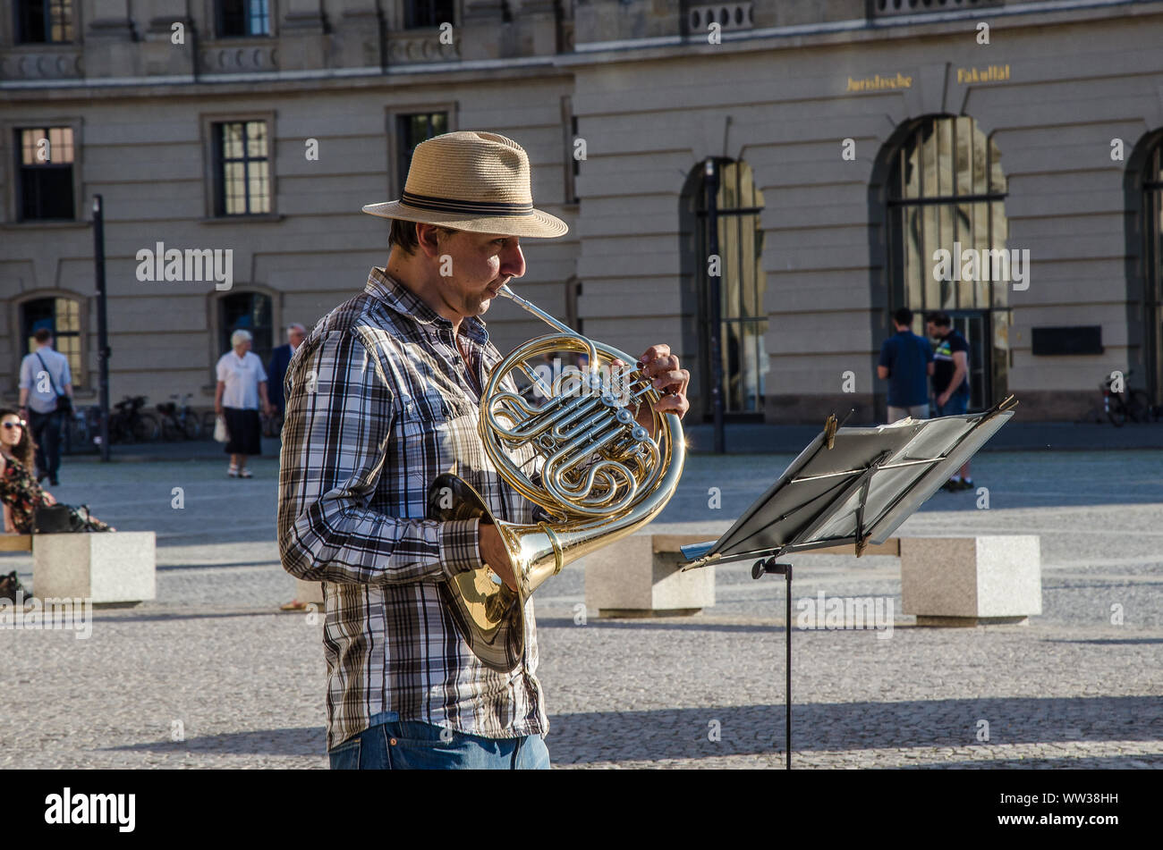 A busker playing the French horn in front of the Berlin Opera house