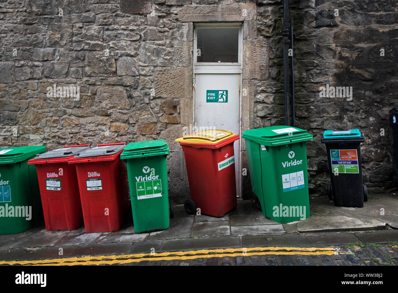 Wheelie bins in an alley with one blocking a fire escape. Stock Photo