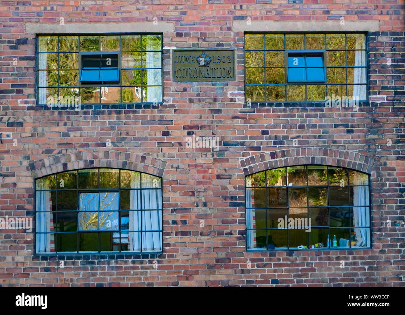 Four iron-framed windows with reflections on the panes of glass in a red brick wall. Stock Photo