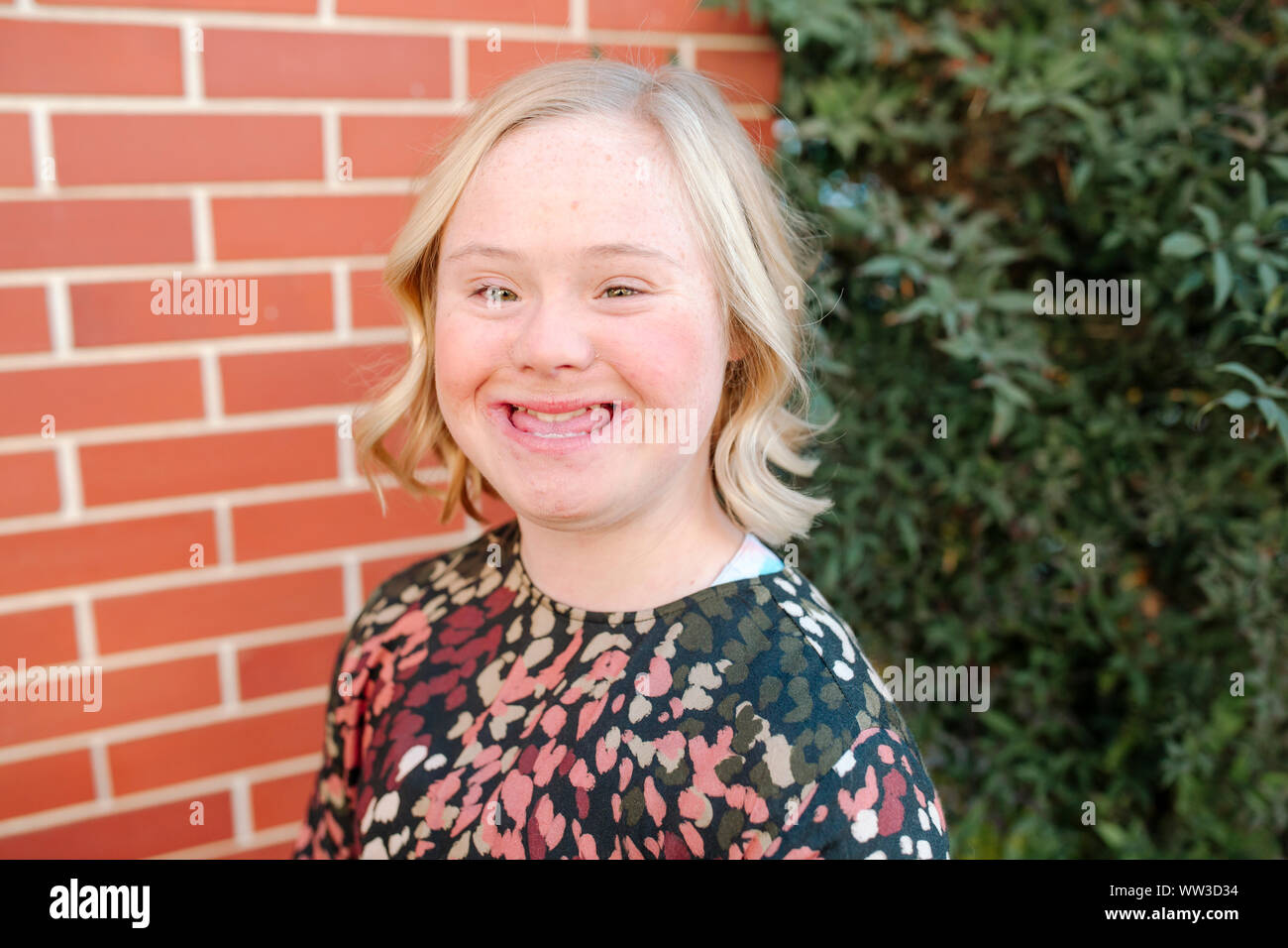 Smiling teen girl with Down Syndrome by brick wall in San Diego Stock Photo