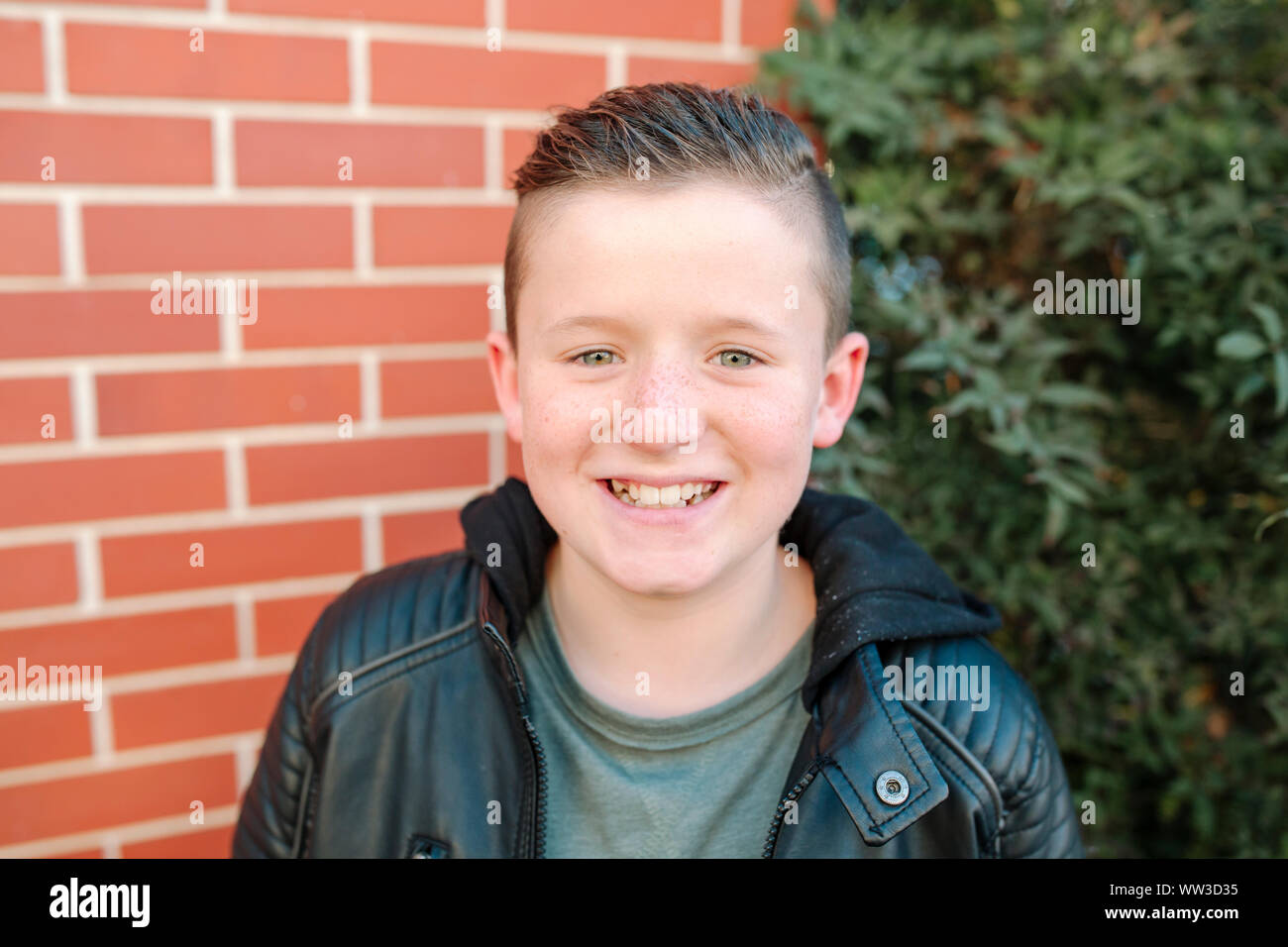 Happy preteen boy smiling in front of brick wall on sunny day Stock Photo