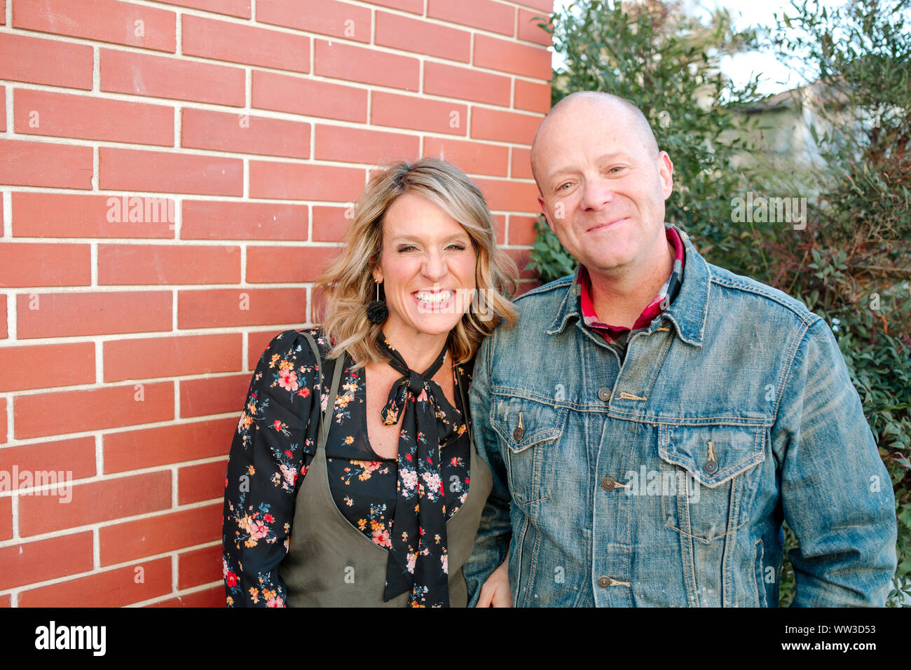 smiling husband and wife standing in front of red brick wall outside Stock Photo
