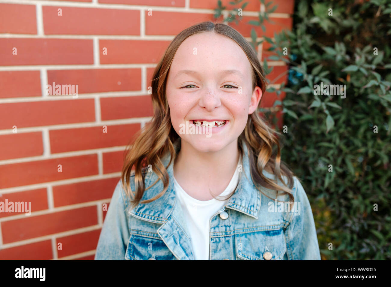 Happy preteen girl wearing denim jacket by brick wall Stock Photo