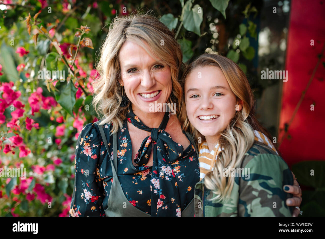 Smiling mother and daughter in front of red flowers on sunny day Stock Photo