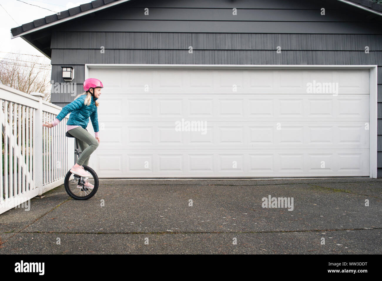 Young Girl Riding Unicycle in Driveway on an Overcast Day Stock Photo