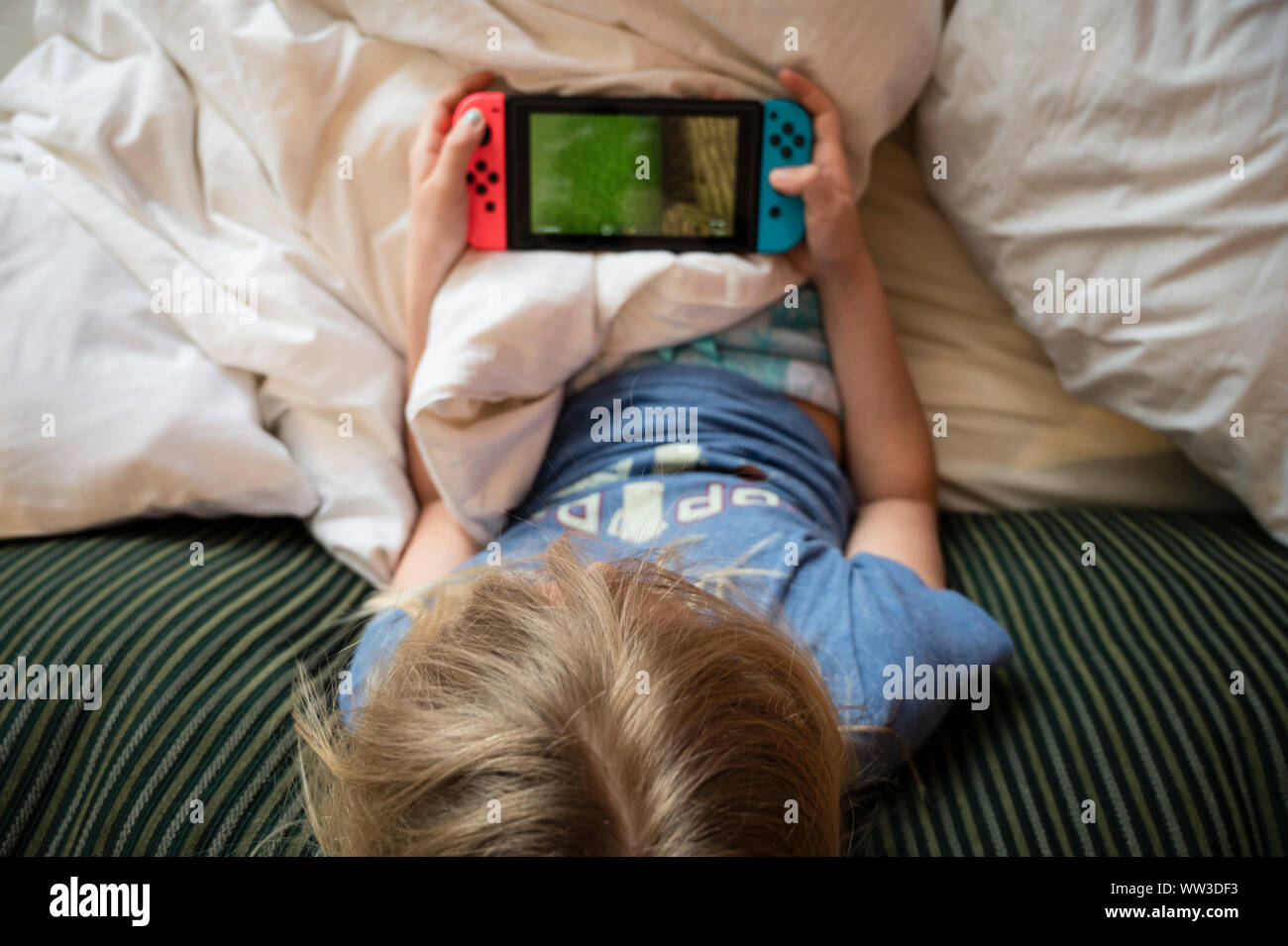 Child Lounging in Bed Playing Hanheld Video Game Stock Photo - Alamy