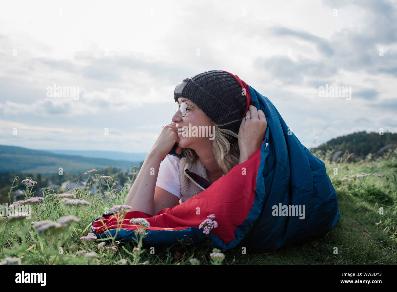 woman laying in sleeping bag on a mountain looking at the view smiling