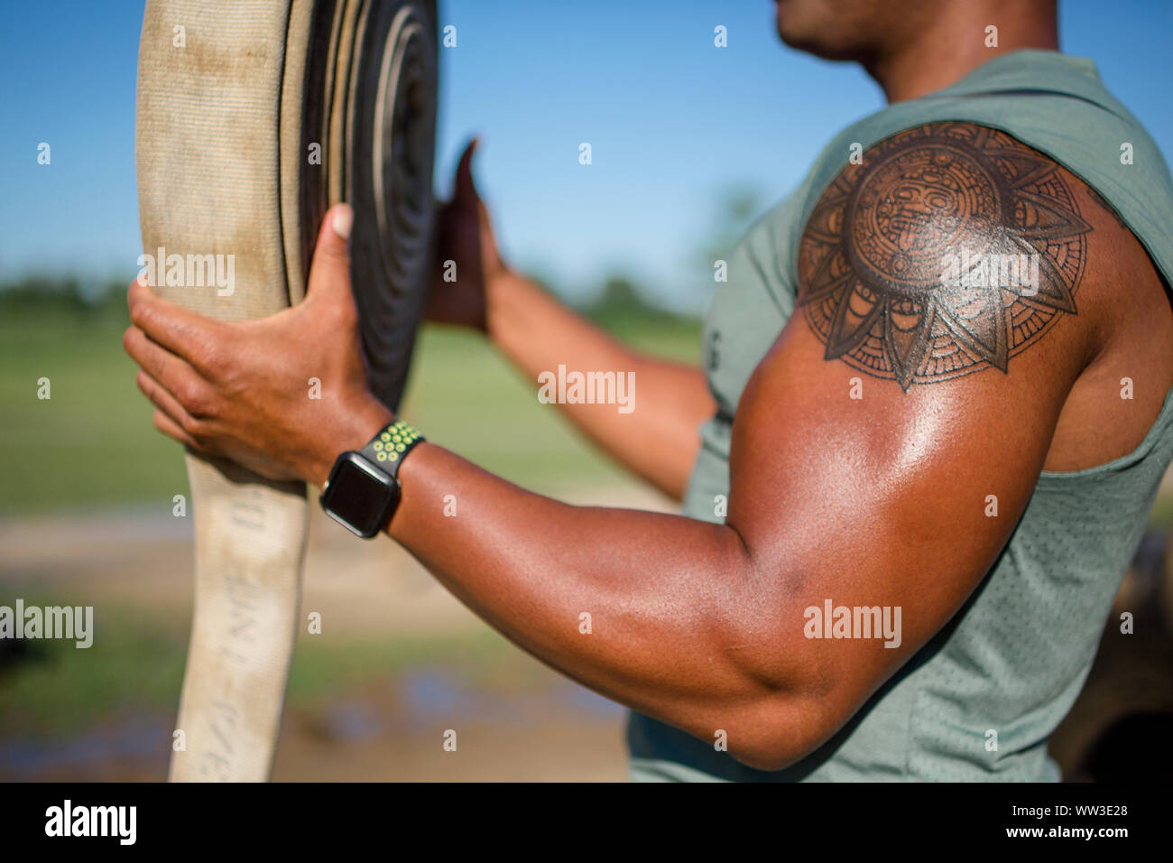 A strong man flexes his bicep and holds a fraying piece of firehose Stock Photo